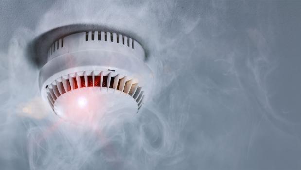 Rauchmelder an der Decke mit rotem Warnsignal und umgeben von Rauch