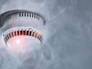 Rauchmelder an der Decke mit rotem Warnsignal und umgeben von Rauch