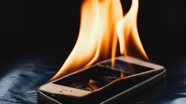 Smartphone mit Flammen, das auf einer dunklen Oberfläche brennt