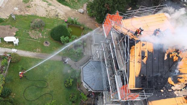 Luftaufnahme eines brennenden Daches mit Feuerwehrleuten und Wasserstrahl