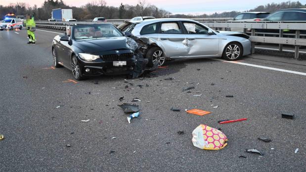 Zwei beschädigte Autos nach einem Unfall auf einer Straße mit Trümmerteilen, Einsatzkräfte im Hintergrund