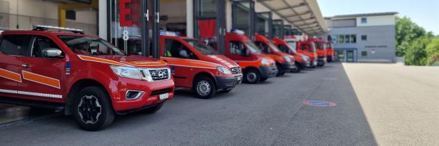 Mehrere rote Feuerwehrfahrzeuge stehen vor einer Feuerwache in Reihe.